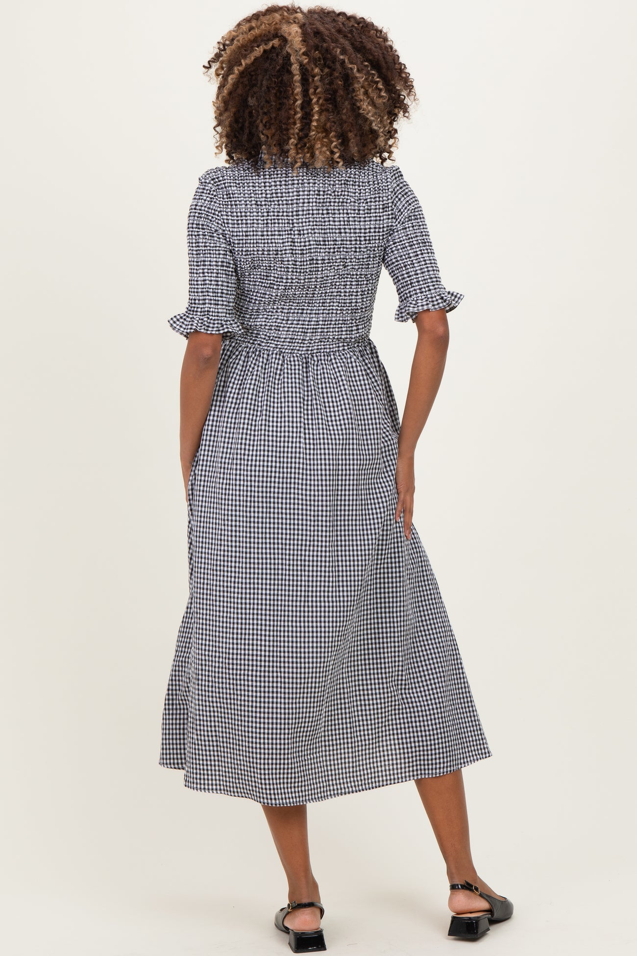 woman wearing a black and white gingham maternity dress with short sleeves and a smocked bodice, standing with her back to the camera