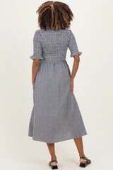 woman wearing a black and white gingham maternity dress with short sleeves and a smocked bodice, standing with her back to the camera