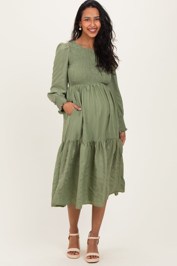woman wearing a dark green long sleeve maternity dress with a flared skirt and pockets, showing her baby bump