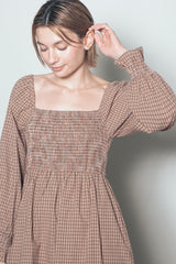 woman wearing a brown checkered smocked dress with long sleeves and a square neckline