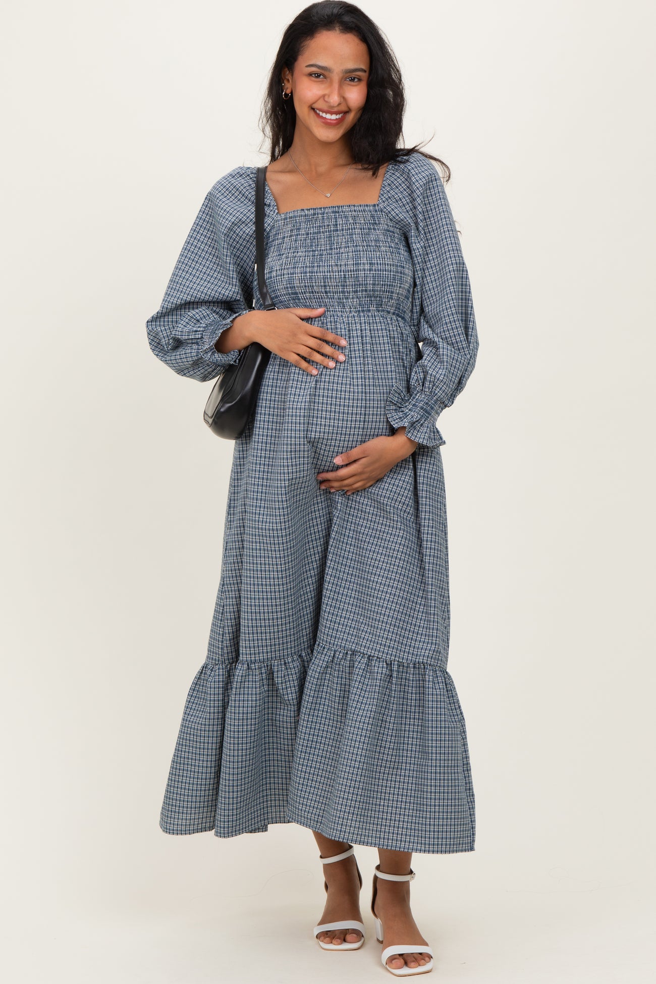 woman wearing a blue and white checkered maternity dress with puff sleeves and a tiered hem, holding her baby bump