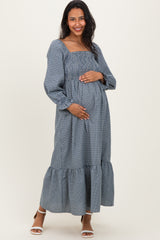 woman wearing a navy and white checkered maternity maxi dress with smocked bodice and ruffled hem, holding her baby bump