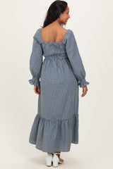 woman wearing a blue gingham maternity dress with a smocked bodice and ruffled hem, showing a pregnant belly