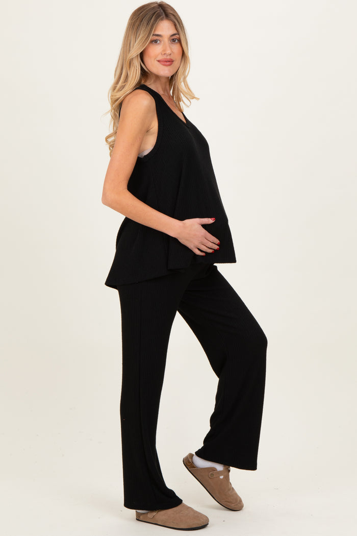 woman wearing a black sleeveless maternity top and matching wide-leg pants, holding her baby bump