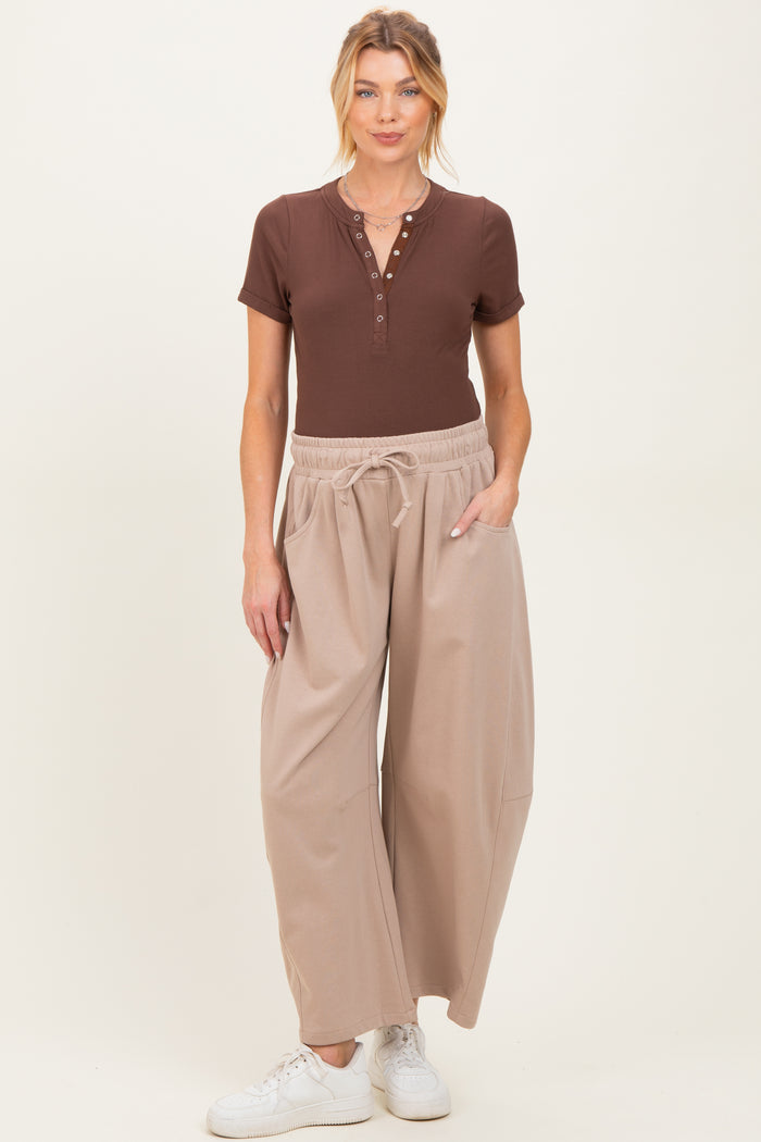 woman wearing a brown short sleeve henley top and light beige wide-leg maternity pants with pockets
