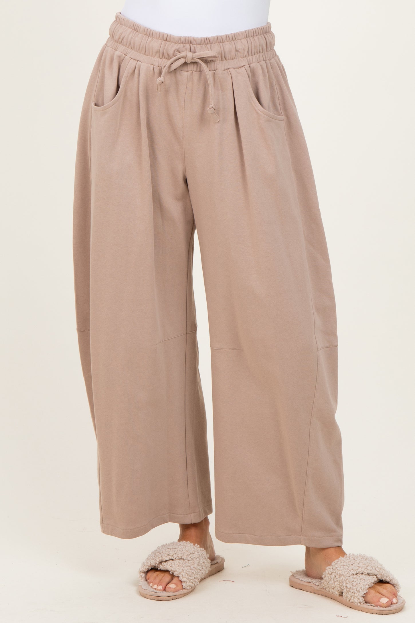 woman wearing light brown wide-leg lounge pants with side pockets and an elastic waist, paired with cozy slippers