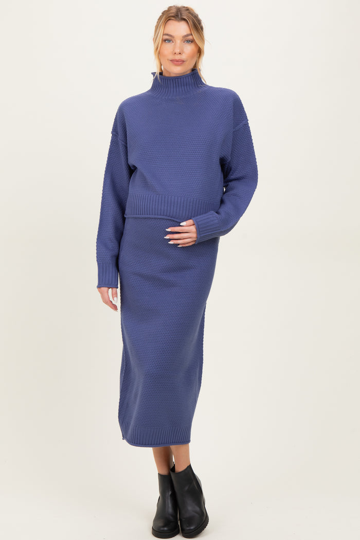 woman wearing a purple maternity sweater and matching midi skirt, holding her baby bump