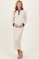 woman wearing a cream maternity maxi dress with a navy collar and buttons, gently cradling her baby bump