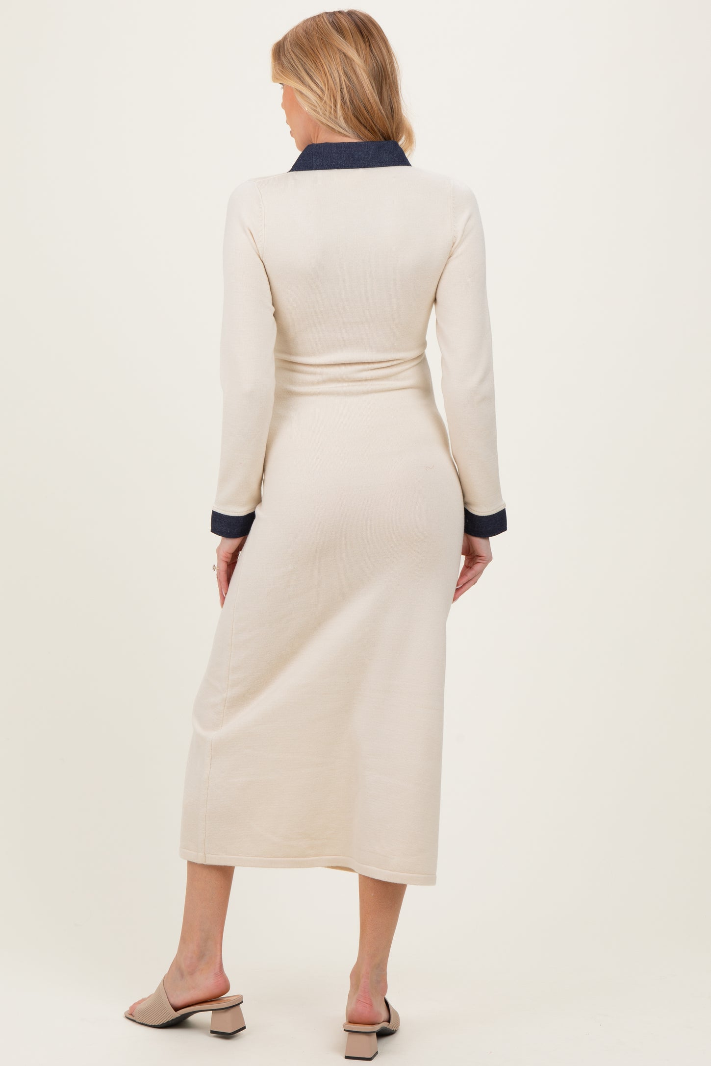woman wearing a cream colored maternity dress with a navy collar and long sleeves, showing a side view of the back