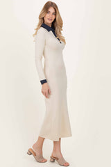 woman wearing a long cream-colored dress with a navy collar and cuffs, paired with beige slip-on sandals