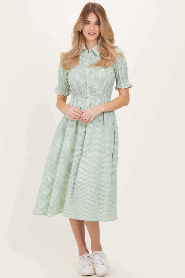 woman wearing a green gingham shirt dress with button detail and short sleeves, paired with white sneakers