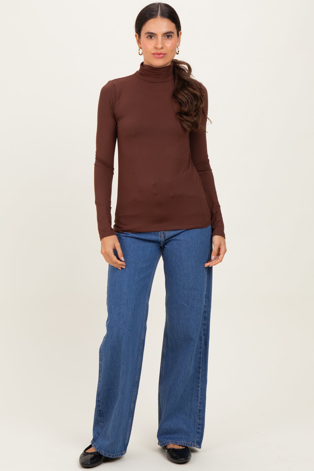 woman wearing a brown long sleeve turtleneck top with blue wide-leg jeans