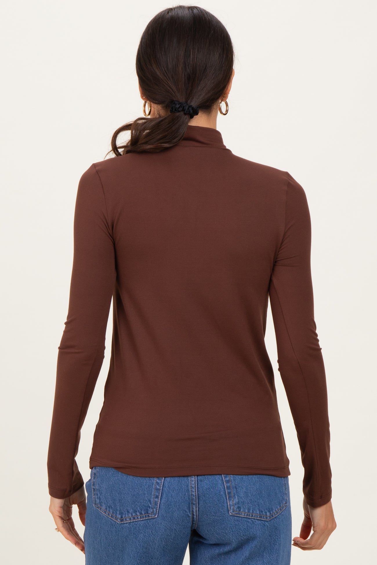 woman wearing a fitted brown long sleeve top with a mock neck and styled hair in a ponytail, viewed from the back