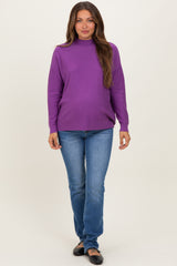woman wearing a purple maternity sweater and blue jeans, with a visible baby bump