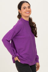 woman wearing a purple long sleeve sweater with a relaxed fit and ribbed hem, smiling and facing slightly to the side