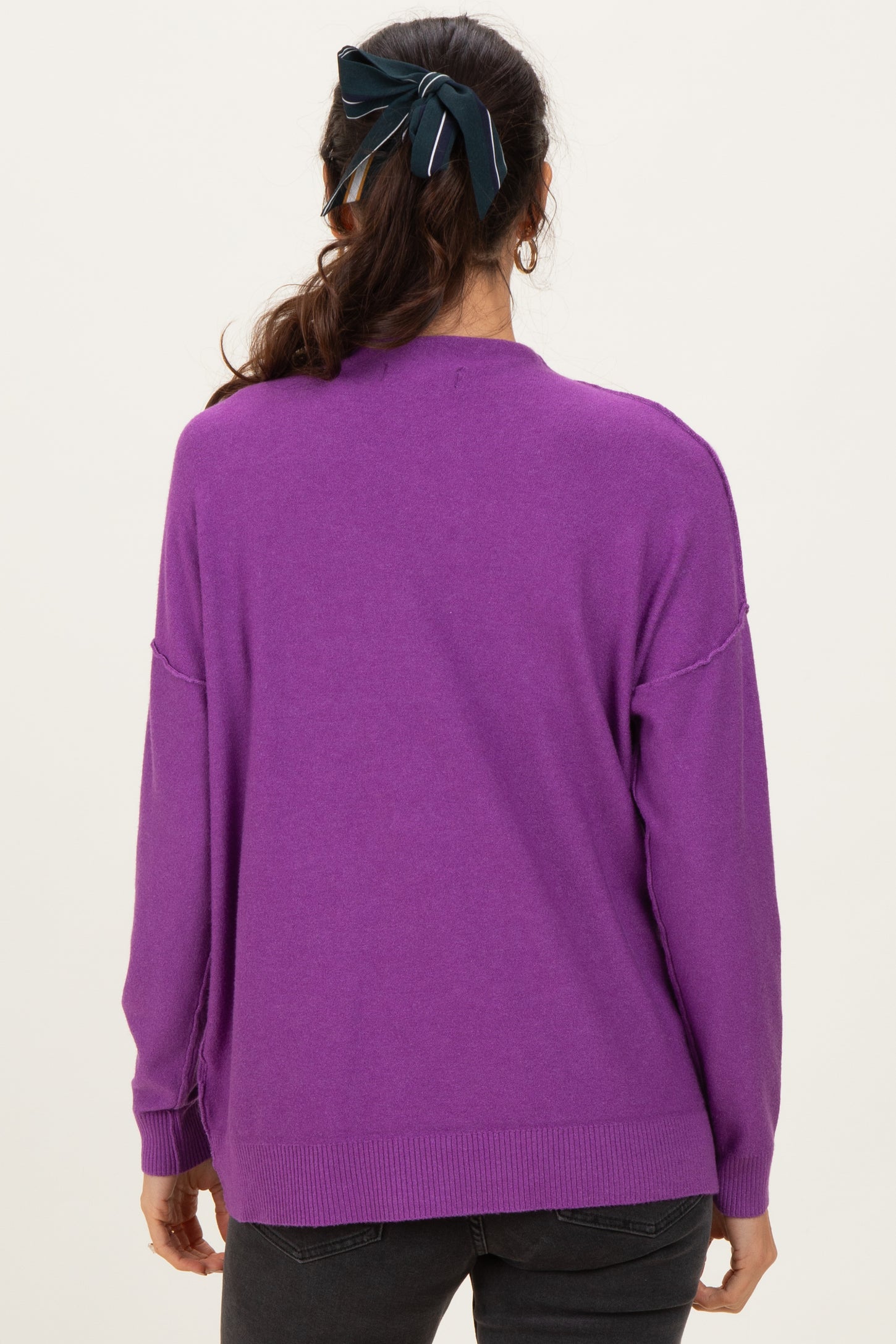 woman wearing a purple oversized sweater, seen from the back, with a hair bow in her dark hair