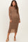 woman wearing a light brown long sleeve maternity dress with ruching detail and a sheer bottom, showing her baby bump