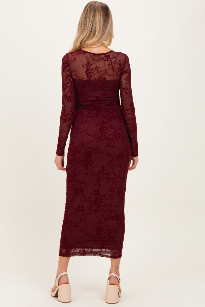 woman wearing a burgundy long sleeve maternity dress with floral lace detailing and a fitted silhouette