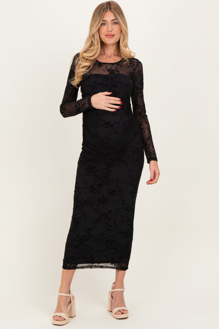 woman wearing a black floral lace maternity dress with a fitted silhouette and long sleeves, holding her baby bump