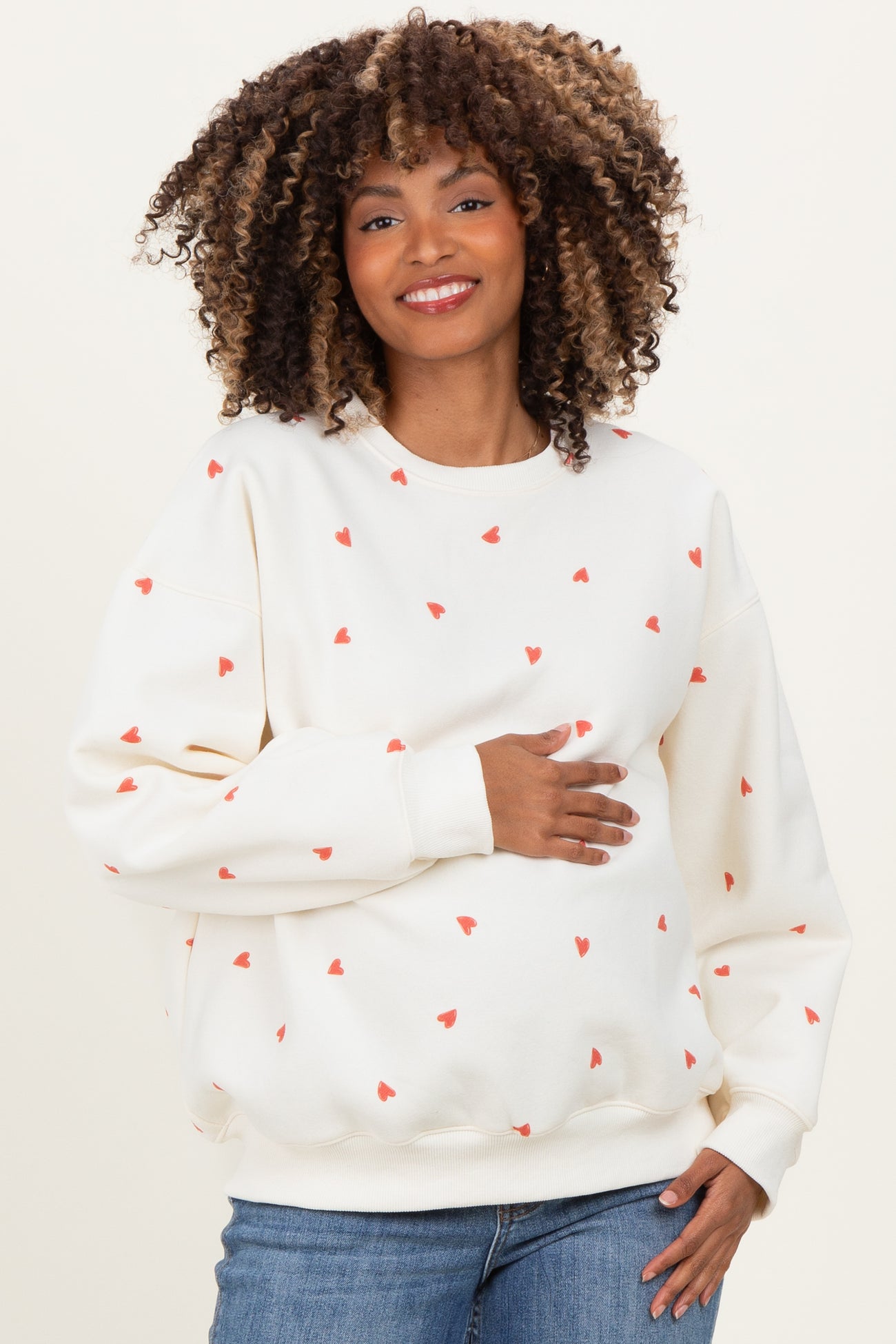 woman wearing a cream maternity sweatshirt with red heart prints and holding her baby bump