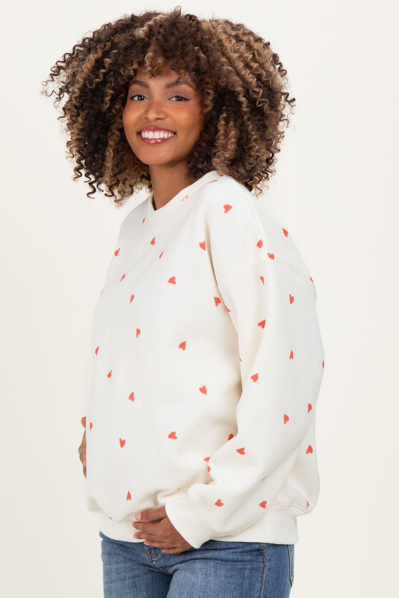 woman wearing a white maternity sweatshirt with red heart prints and a visible baby bump