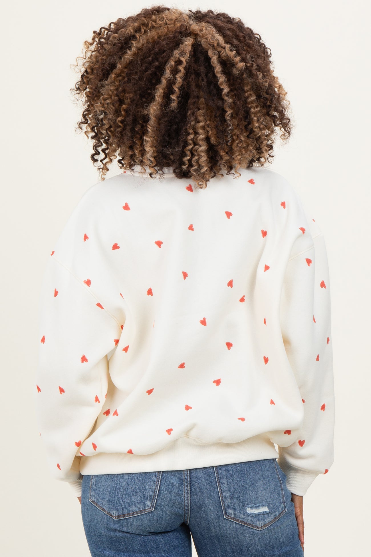 woman wearing a cream maternity sweatshirt with small red heart prints, viewed from the back, paired with blue jeans