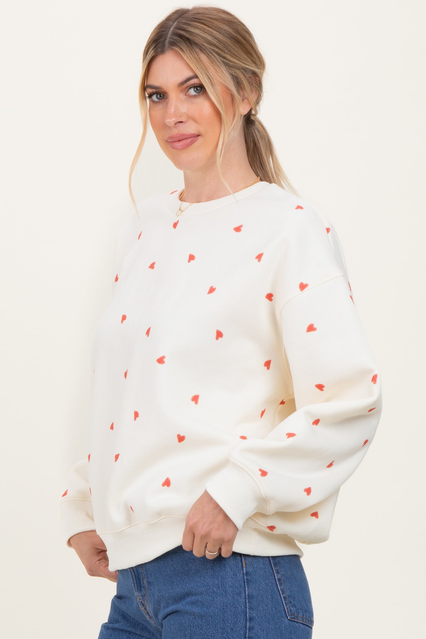 woman wearing a cream sweatshirt with red heart patterns and relaxed fit, styled with blue jeans