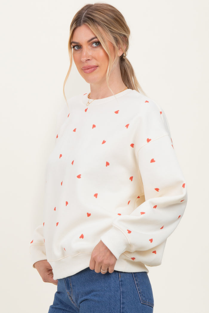 woman wearing a cream sweatshirt with red heart patterns and relaxed fit, styled with blue jeans
