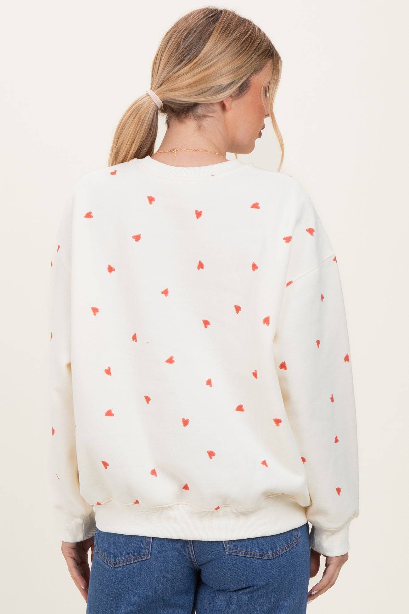 woman wearing a cream oversized sweatshirt with red heart print, viewed from the back