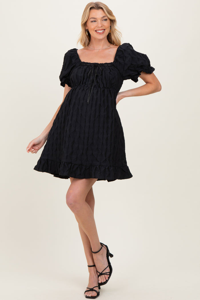 woman wearing a black maternity dress with puff sleeves and ruffled hem, styled with strappy black heels