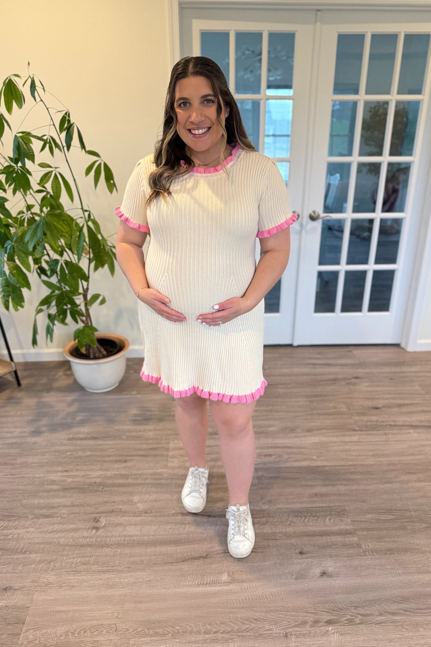 woman wearing a cream ribbed maternity dress with pink ruffle trim and a visible baby bump