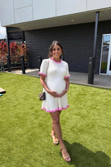 woman wearing a cream ribbed maternity dress with pink ruffled sleeves and hem, showing her baby bump