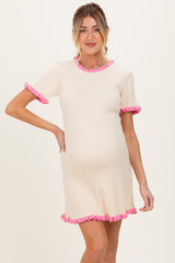 woman wearing a cream ribbed maternity dress with pink ruffle trim and a visible baby bump