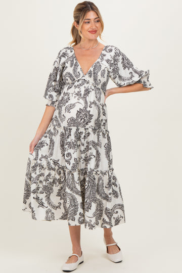 woman wearing a black and white printed maternity dress with a v-neck and tiered skirt, holding her baby bump