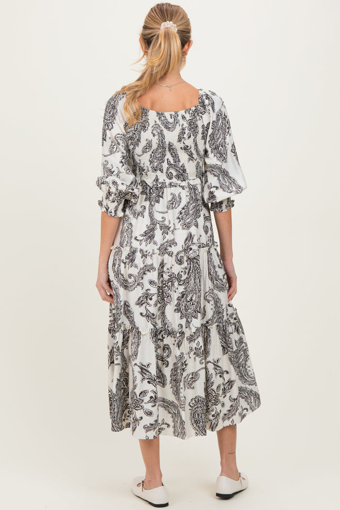 woman wearing a black and white paisley print maternity dress with a tiered skirt and puff sleeves, showing her baby bump