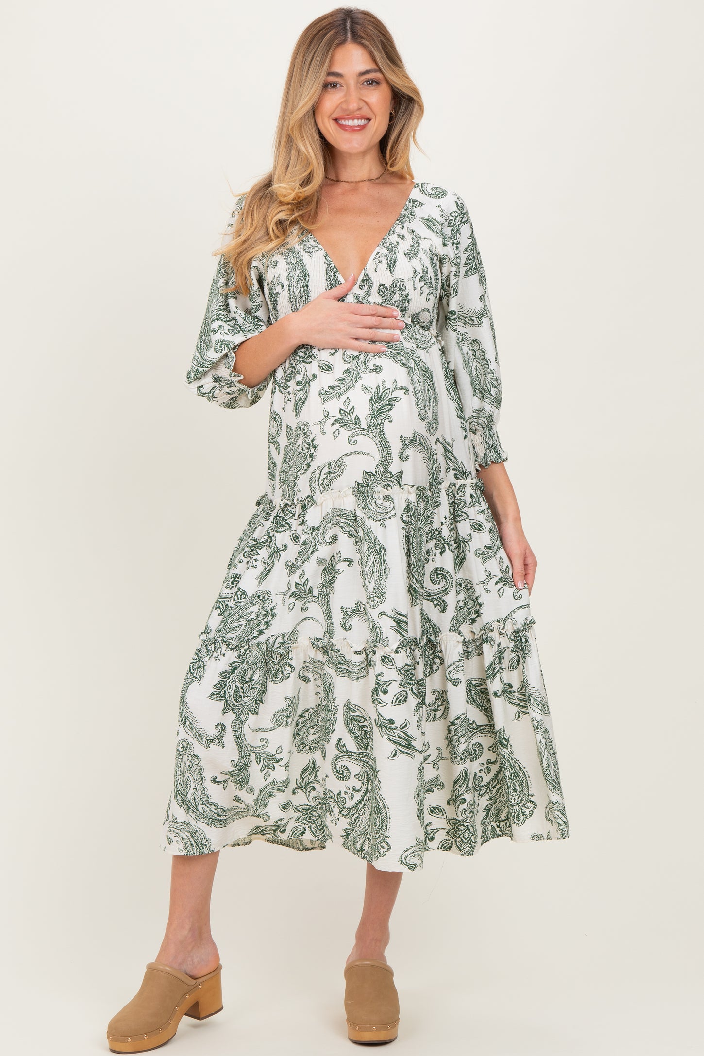 woman wearing a green and white patterned maternity dress with a v-neck and three-quarter sleeves, holding her baby bump