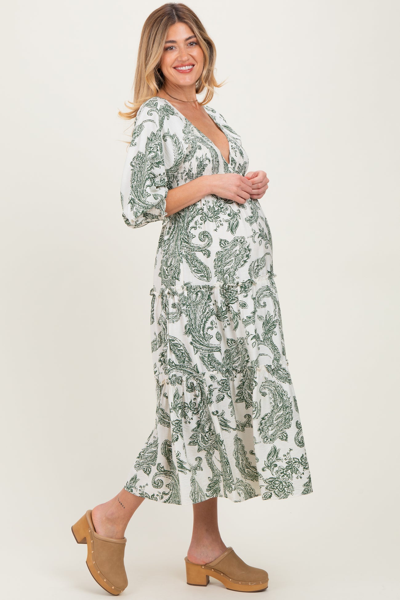 woman wearing a white maternity dress with green paisley print and a visible baby bump