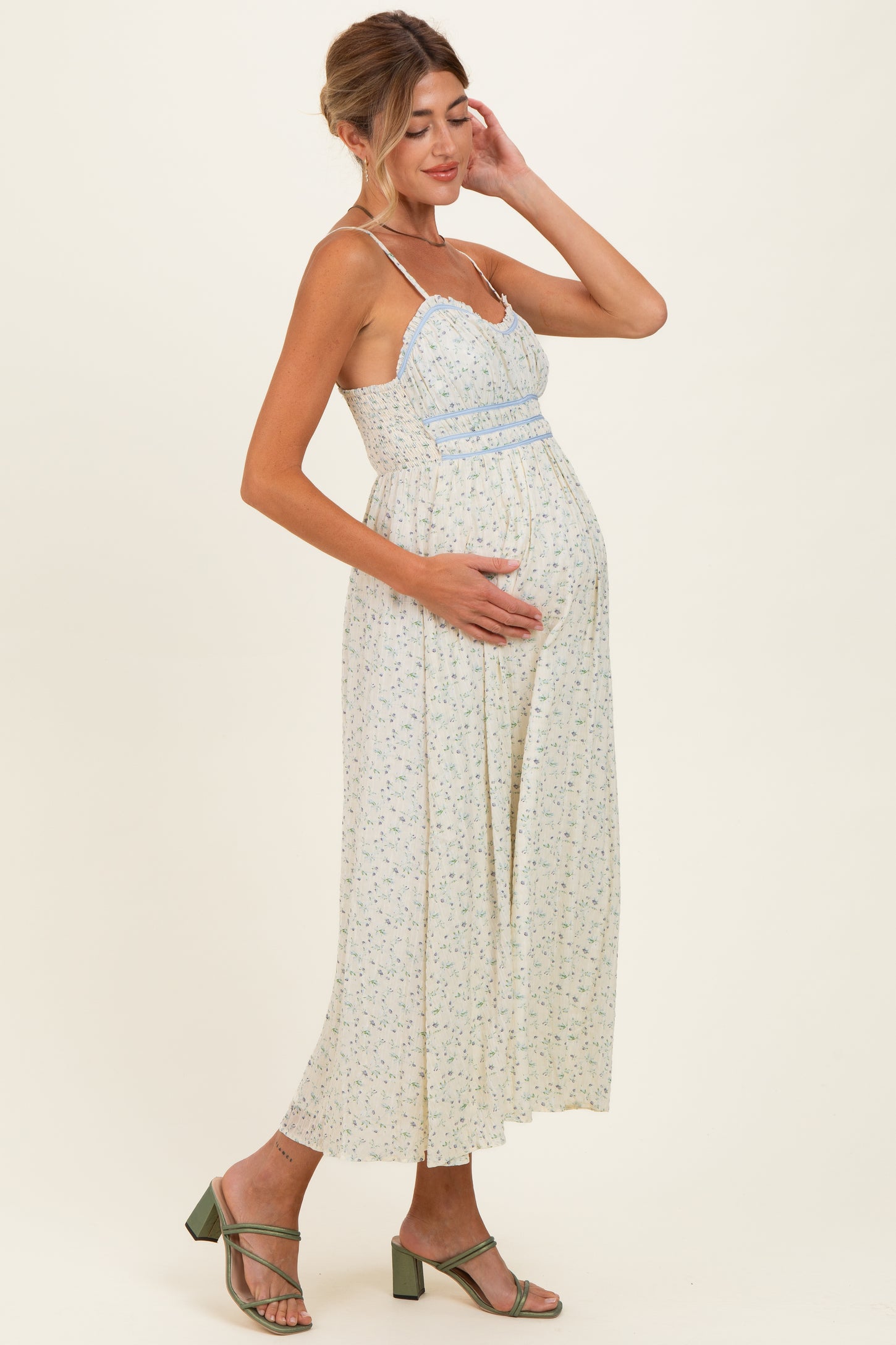 woman wearing a light floral maternity maxi dress and cradling her baby bump