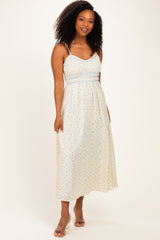 woman wearing a floral midi dress with thin straps and an elasticized waist, styled with a light color palette