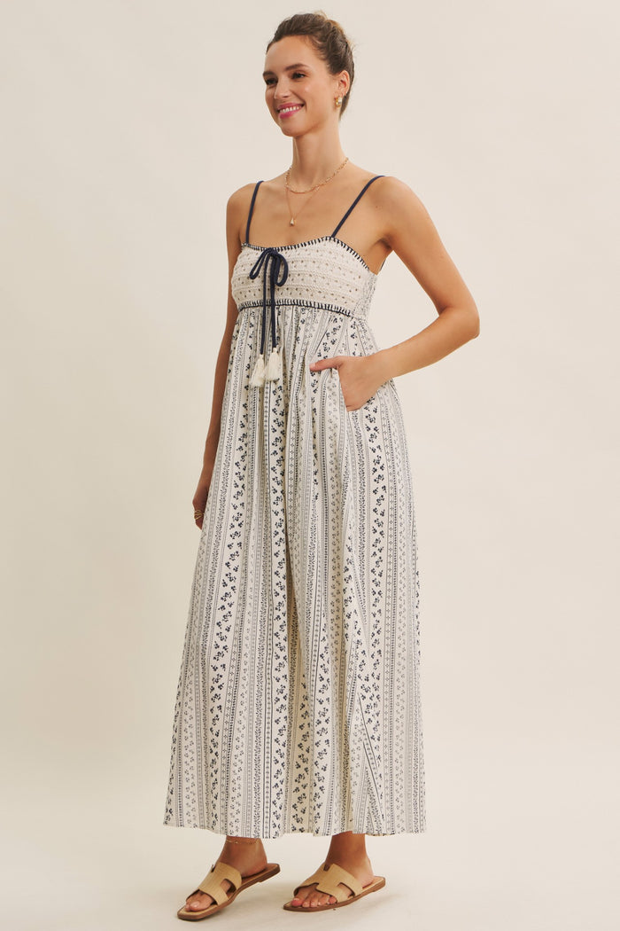 woman wearing a white patterned maxi dress with a smocked bodice and tie detail, featuring pockets and slide sandals