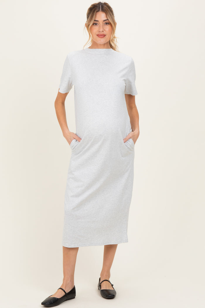 woman wearing a light grey short sleeve maternity dress with pockets and a baby bump visible