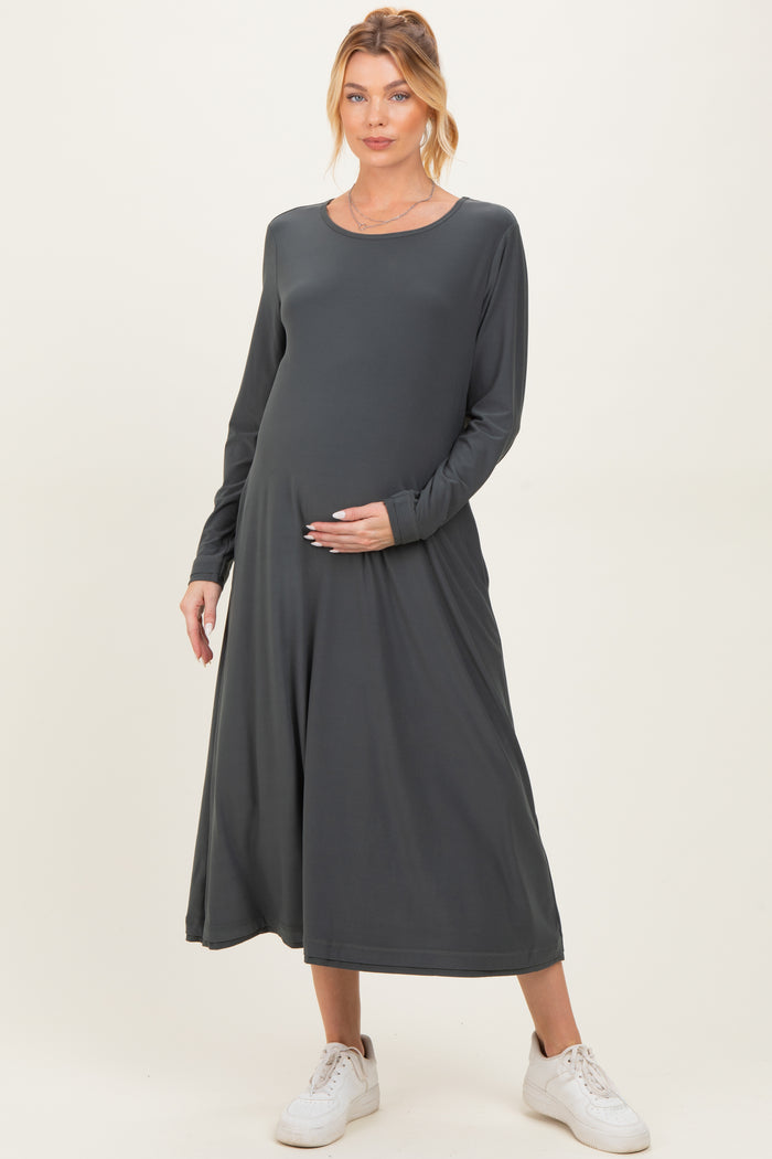 woman wearing a dark gray long sleeve maternity dress, gently cradling her baby bump