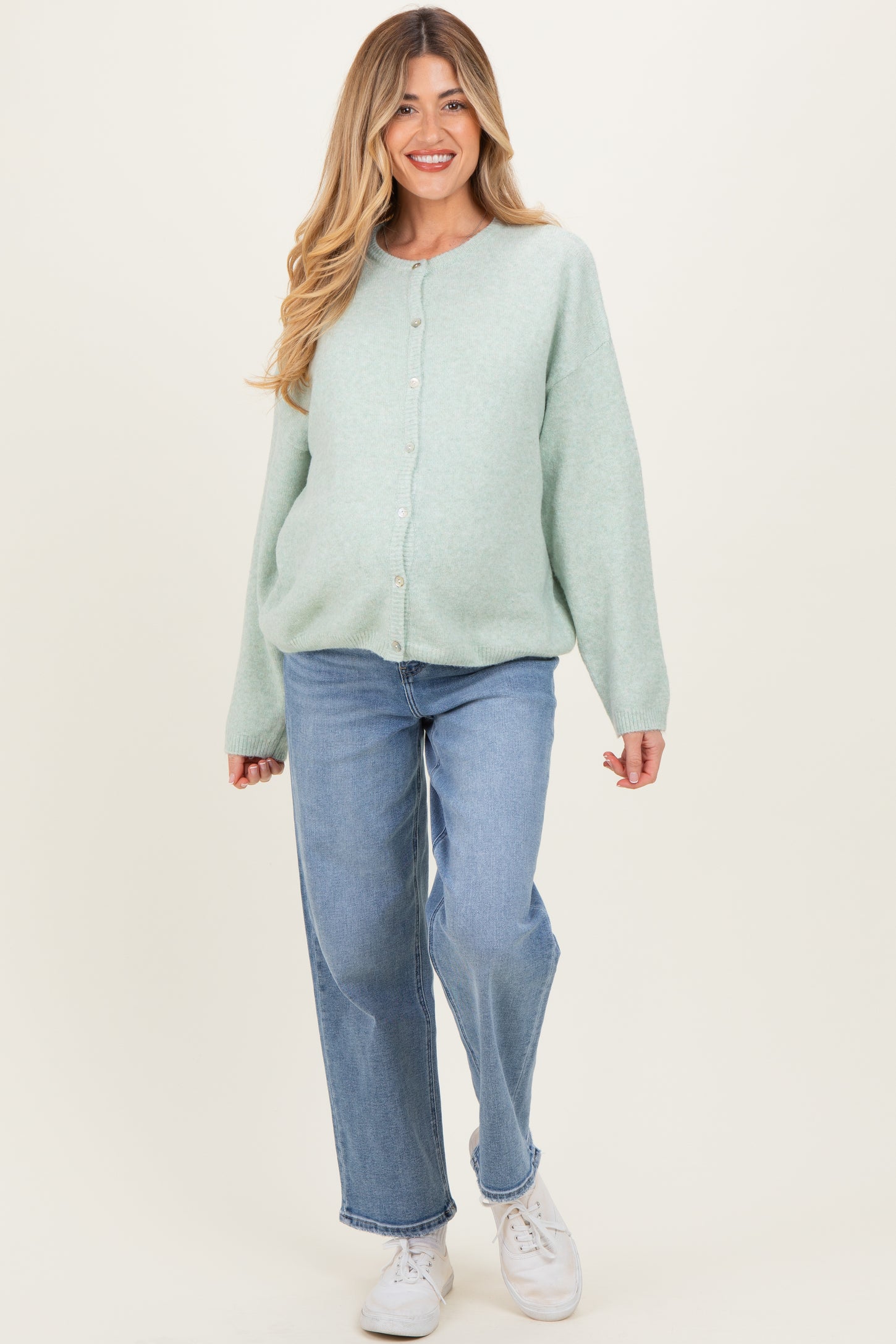 woman wearing a mint green button-up maternity cardigan with a visible baby bump and paired with light blue jeans