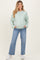 woman wearing a light green maternity cardigan with buttons and pockets, paired with wide-leg jeans and sneakers