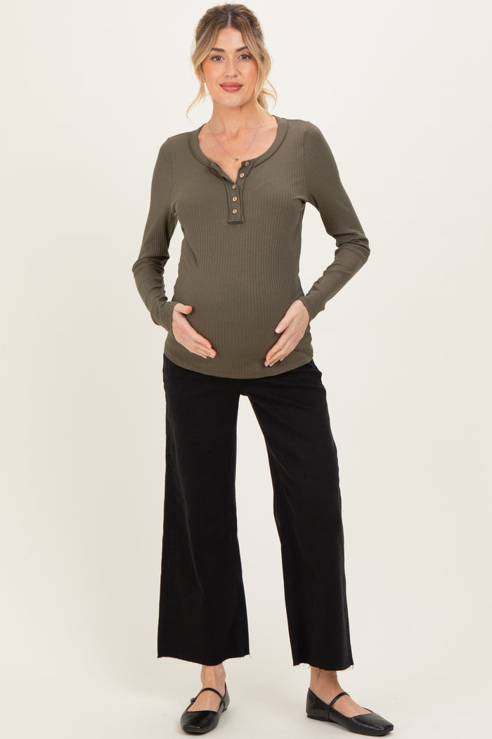 woman wearing a dark green long sleeve maternity top with buttons and black wide-leg pants, gently cradling her baby bump