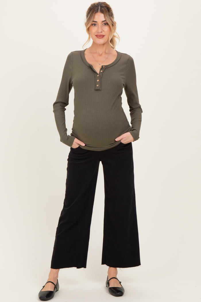 woman wearing an olive green long sleeve maternity top with buttons and black wide-leg pants, holding her baby bump