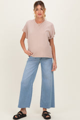 woman wearing a blush pink maternity top and high-waisted wide-leg jeans, posing with one hand on her hip
