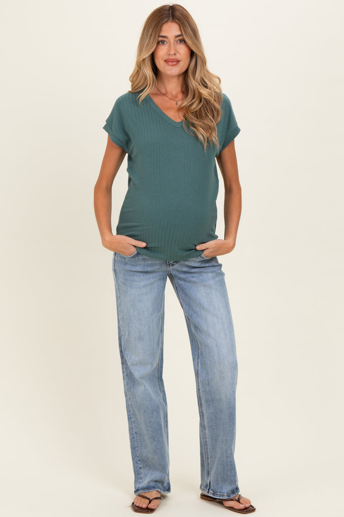 woman wearing a teal v-neck maternity top and light blue jeans, showing a baby bump
