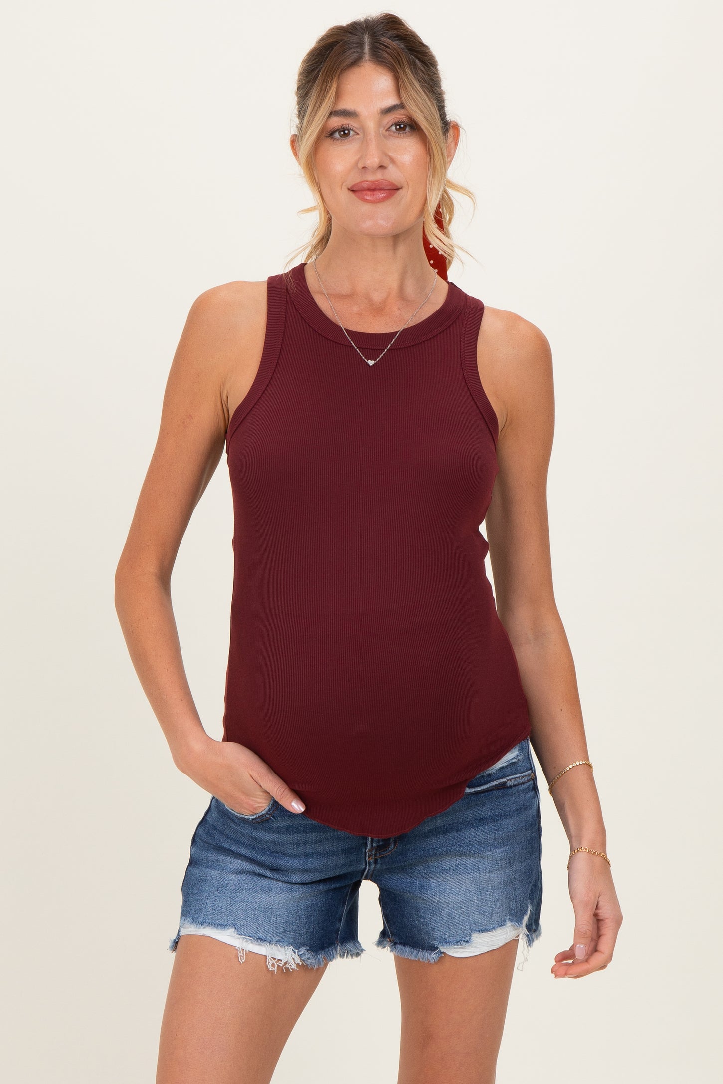 woman wearing a burgundy ribbed maternity tank top and denim shorts with a visible baby bump