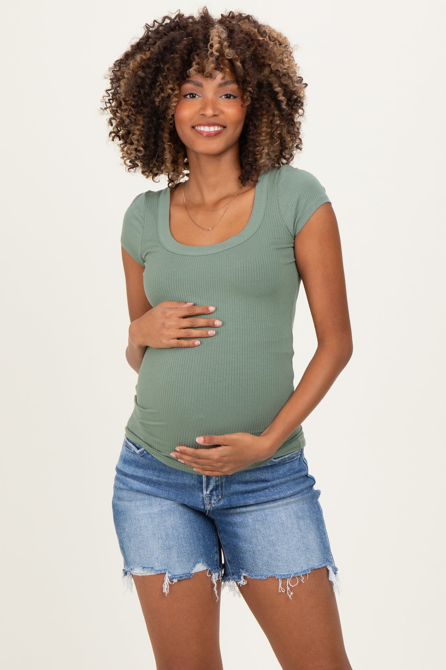 woman wearing a green ribbed maternity top and denim shorts, showcasing her baby bump